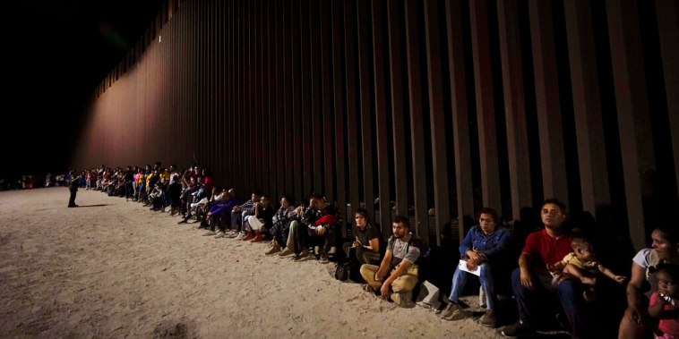 Inmigrantes esperan a lo largo de la valla que divide la frontera entre Estados Unidos y México, cerca de Yuma, en Arizona, el 23 de agosto de 2022.
