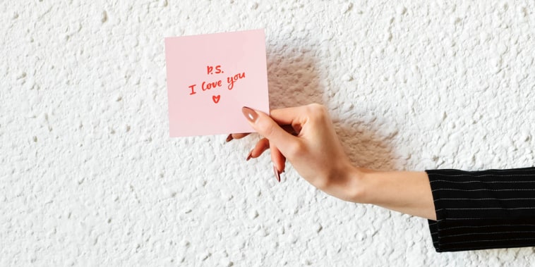 The girl holds in her hand a pink love note. Valentine's Day. White background. Woman's hand. Declaration of love. Love note. Confession note.