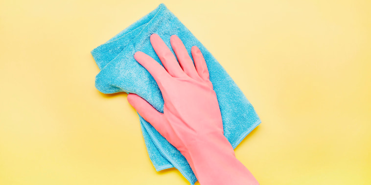 Hand in pink glove with cleaning rag on yellow background