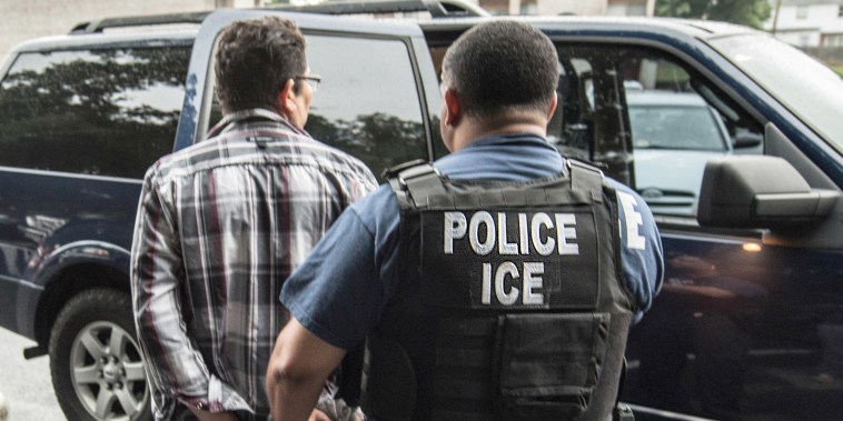 A suspect is escorted by an ICE agent for transportation