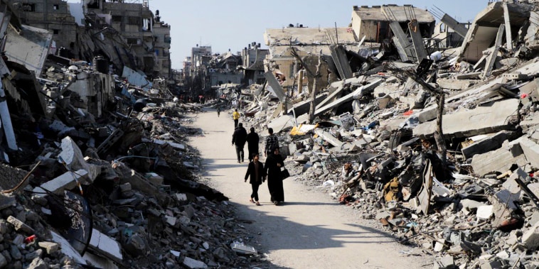 Palestinians walk through the destruction from the Israeli offensive