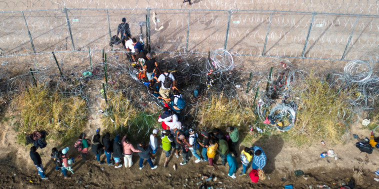 An aerial view of migrants passing through coils of razor wire while crossing the U.S.-Mexico border