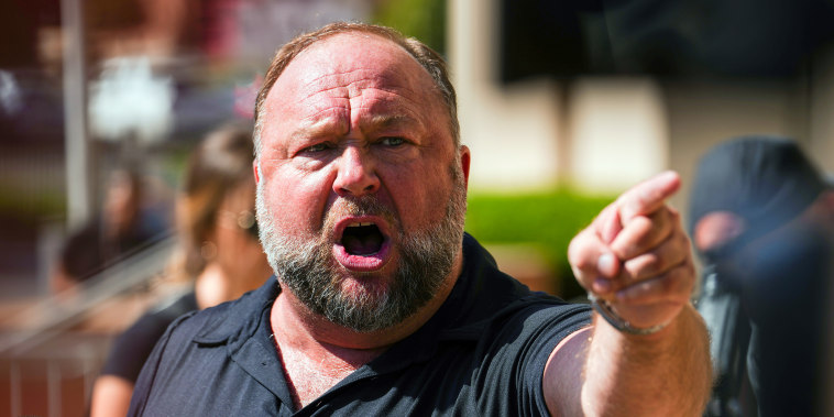 Alex Jones points as he speaks to the media outside the courthouse.