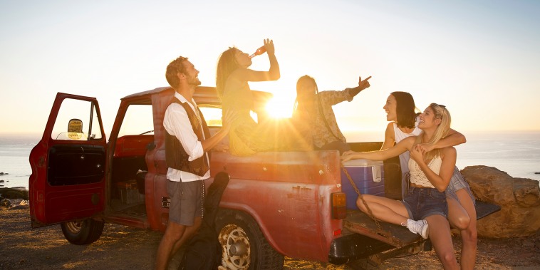 Happy young people outside pick up truck at the coast at sunset