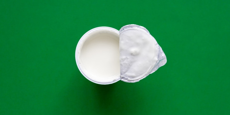 An opened plastic yogurt cup on a green background