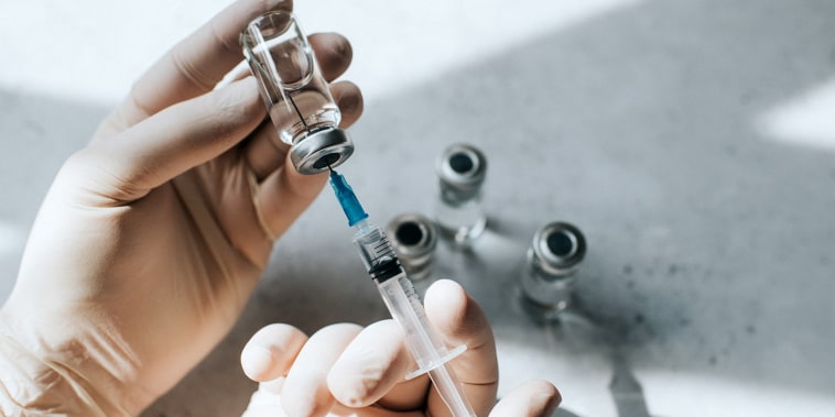 Gloved hand holds a syringe and a  vial