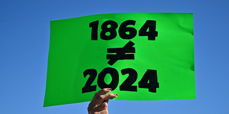A woman holds a sign that says 1864 different from 2024