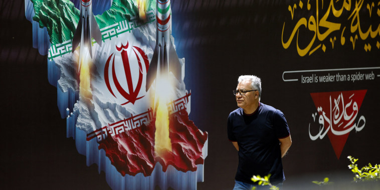A man walks past a banner depicting missiles along a street in Tehran 