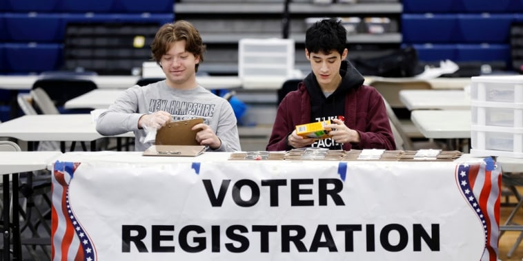Los estudiantes de secundaria Sawyer Brockman, izquierda, y Jack Skilling son voluntarios en la mesa de registro de votantes para las elecciones primarias presidenciales en Windham High School, el martes 23 de enero de 2024, en Windham, Nuevo Hampshire
