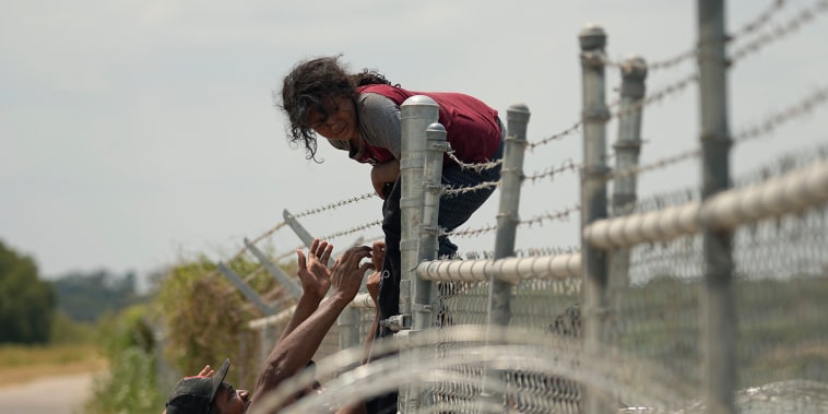 Migrantes que cruzaron el río Bravo desde México hacia Estados Unidos escalan por  una cerca con alambre de púas, el lunes 21 de agosto de 2023, en Eagle Pass, Texas.