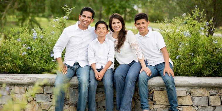 Latin family of four sitting on low wall and smiling