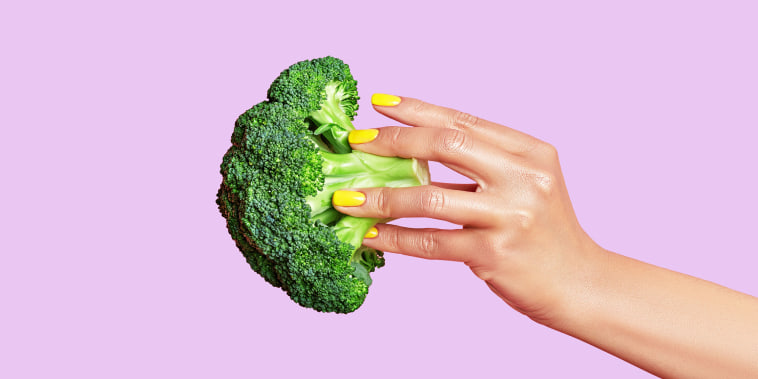 Cropped hand of woman holding broccoli against pink background