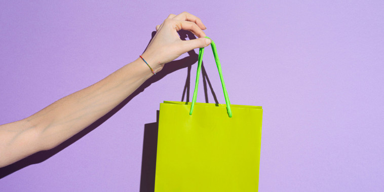 Woman's hand carrying colorful goody bag on lilac background