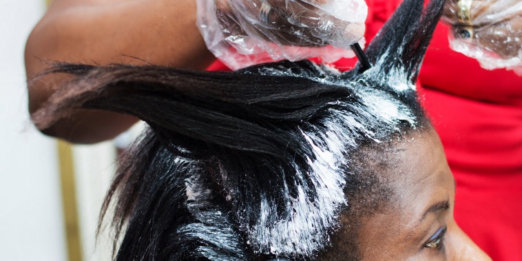 A hairdresser applies hair relaxer to a black woman's roots