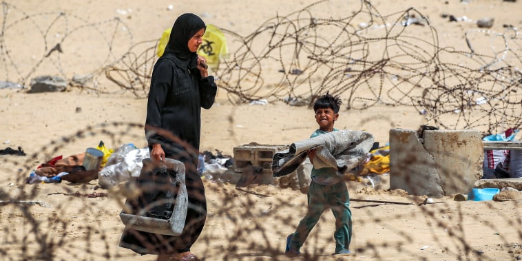 A woman and boy walk with belongings past barbed-wire fences as they flee from Rafah 