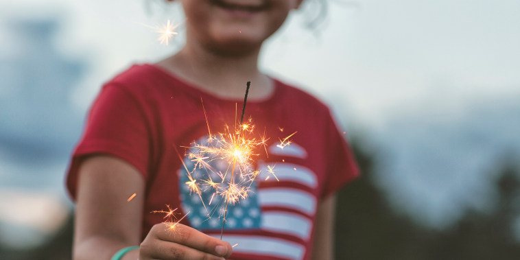 Midsection view of girl holding a lit sparkler with heart-shaped American flag t-shirt on.