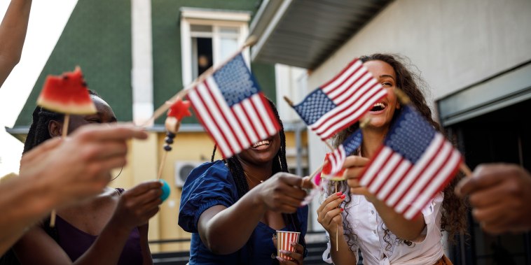 Candid shot of diverse group of joyful young people, friends, having fun, dancing and waving American flags while celebrating 4th of July on the balcony.