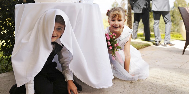 Two kids hiding underneath a table at a wedding.