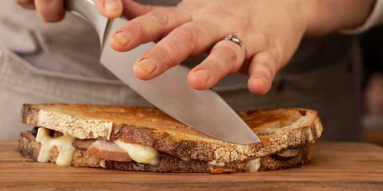 Close up of person slicing toasted sourdough cheese melt with chef's knife.