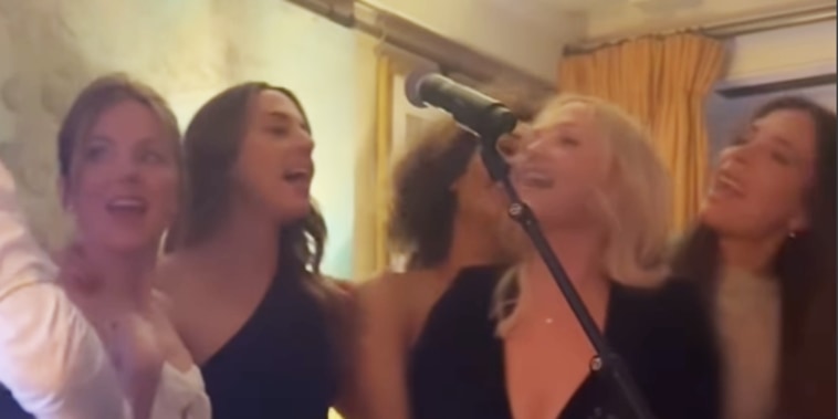 The Spice Girls in cocktail attire sing in as a man strums a guitar.