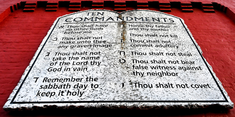 A stone table with the ten commandments listed on it, attached to the side of a red building exterior wall