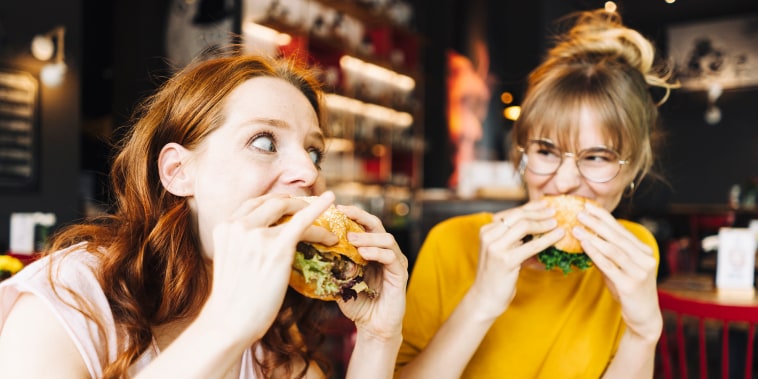 Two female friends eating burger in a restaurant.