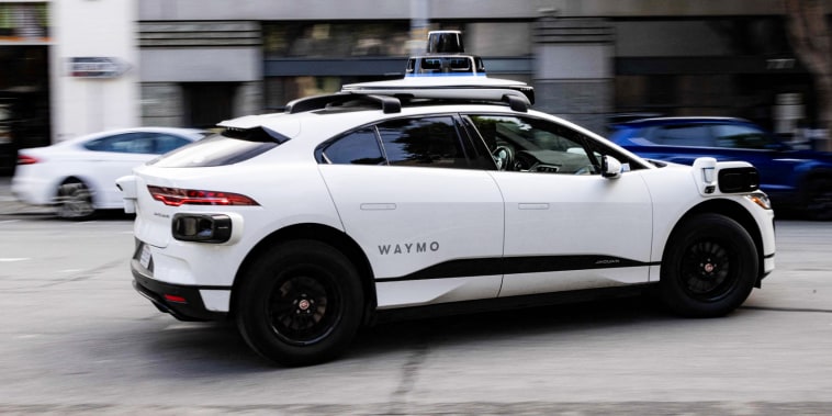 A white Waymo robotaxi vehicle driving on the street