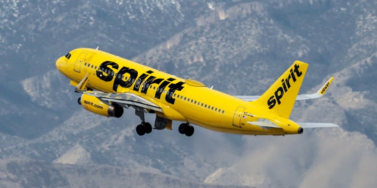 A Spirit Airlines plane flies near a mountain scape