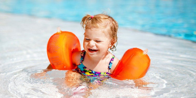 Little toddler girl wearing arm floaties in outdoor swimming pool.
