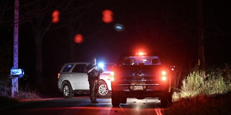 An armed police officer stands on the road with emergency vehicles