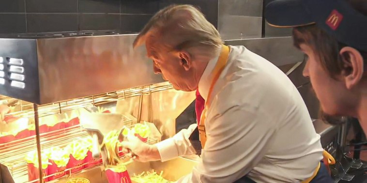 Donald Trump inside of a McDonald's kitchen wearing an apron and loading fries