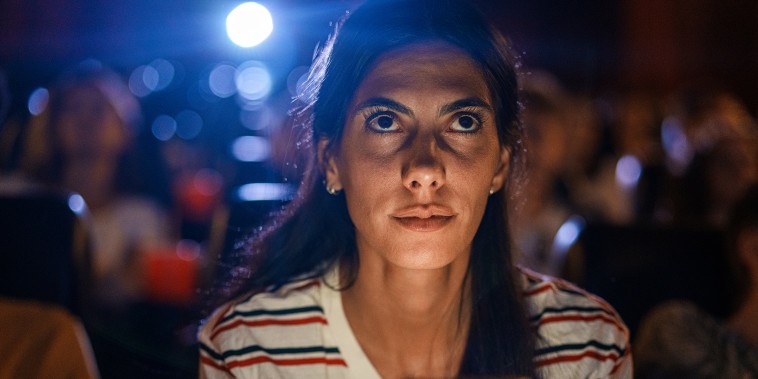 Young woman looking at mobile phone while watching a film inside movie theater