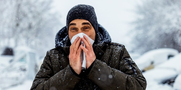 Man blowing his nose in cold, snowy weather outside.