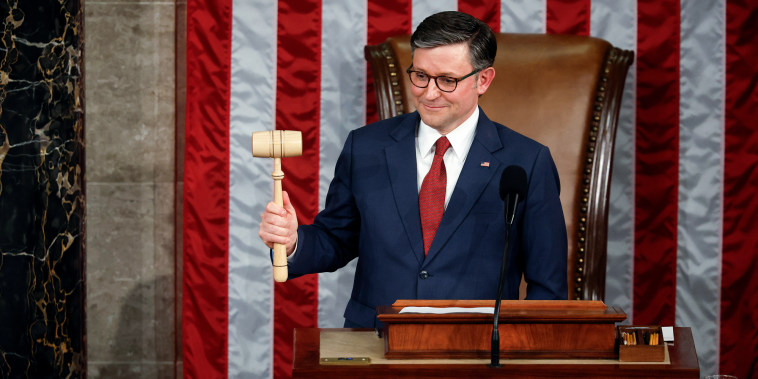 Mike Johnson holds a gavel at a podium, American flag hangs behind him