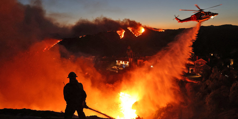 A helicopter drops water as the Palisades Fire grows in Pacific Palisades, Calif., on Jan. 7, 2025. 