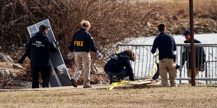 Members of the Federal Bureau of Investigation (FBI) Evidence Response Team move debris near the crash site along the Potomac River