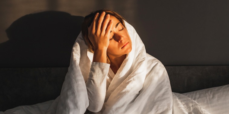 Woman has a headache and sitting in bed covered with blanket.