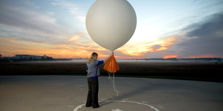 A woman holds a weather balloon on pavement against a dusky sky. 