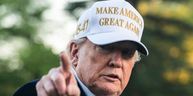 Donald Trump points and wears a white hat that says "Make America Great Again"