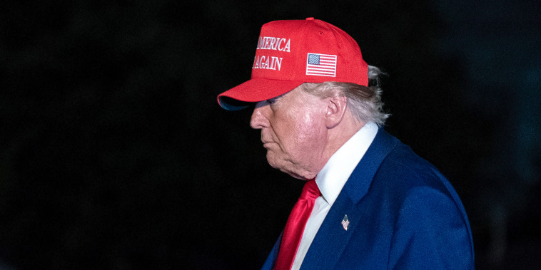 Donald Trump walks outside wearing a red MAGA hat, side profile