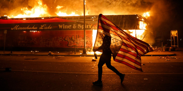 A protester carries a U.S. flag upside down as he walks past a burning building