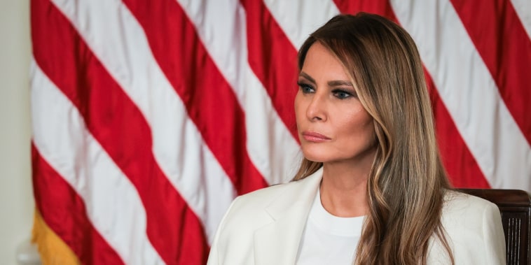 Melania Trump seated in front of an American flag backdrop