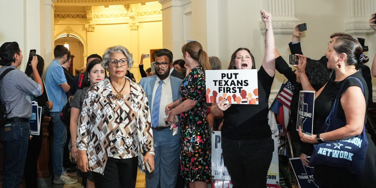Senfronia Thompson, left, walks past a crowd of people into the House Chamber, a person holds a sign that says "put Texans first"