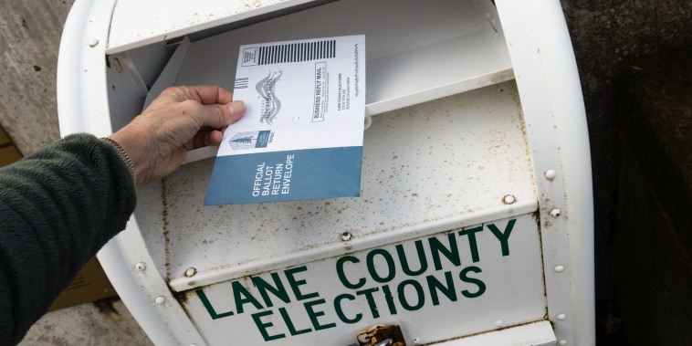 A hand hovers a ballot over a ballot drop box