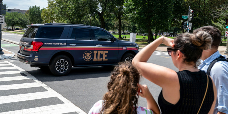An Immigration and Customs Enforcement police SUV patrols on the road as people watch from the sidewalk