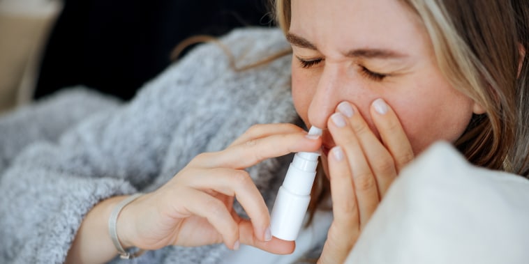 Sick young woman using nasal spray