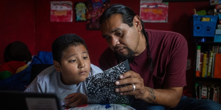 Evan Torres looks at a journal with Robert while seated on a bed
