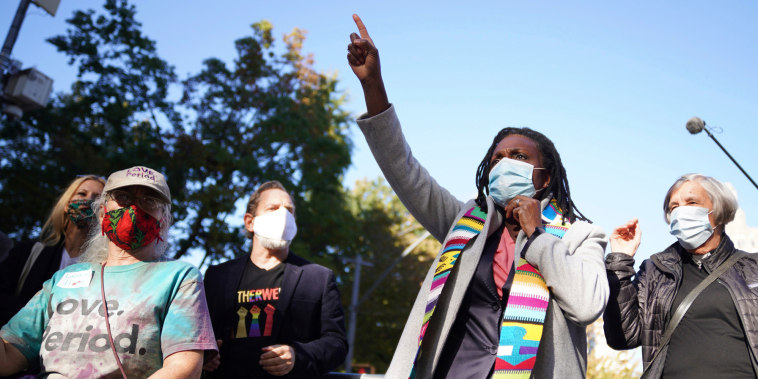 Jacqui Lewis speaks outside while wearing a facemask, point upwards
