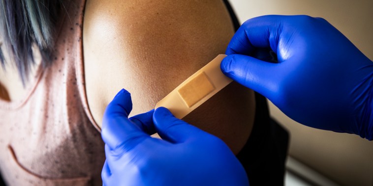Blue gloved hands place a bandaid on someone's arm