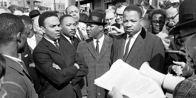 A federal marshal reads a court order halting a planned voter registration protest as Dr. Martin Luther King Jr., right, and fellow marcher Andrew Young, left, look on.